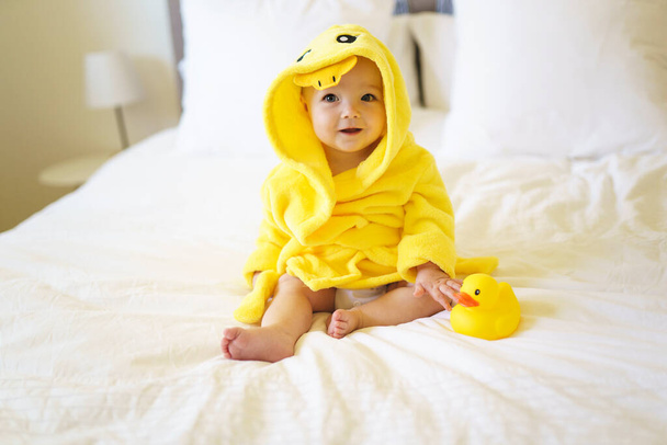 Baby wearing yellow bathrobe duck on parents bed after bath - 写真・画像