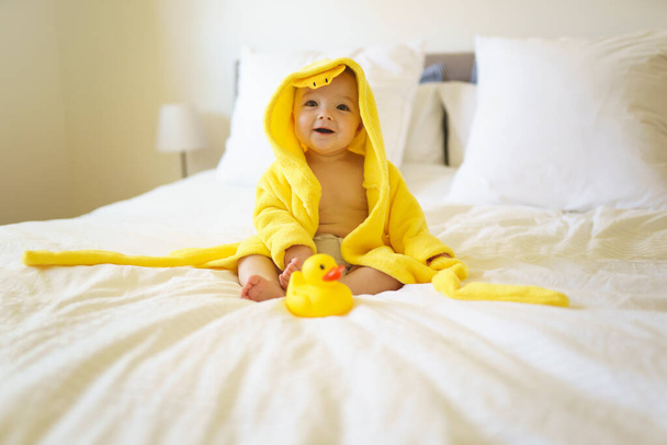 Baby wearing yellow bathrobe duck on parents bed after bath - Photo, Image