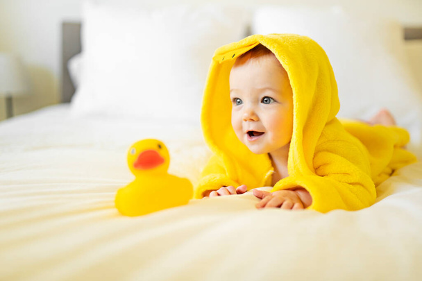 Baby wearing yellow bathrobe duck on parents bed after bath - Foto, afbeelding