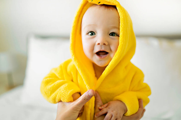 Baby wearing yellow bathrobe duck on parents bed after bath - Foto, afbeelding