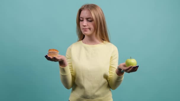 Jonge vrouw kiezen tussen appel en cupcake, het meisje is kiezen cupcake. - Video