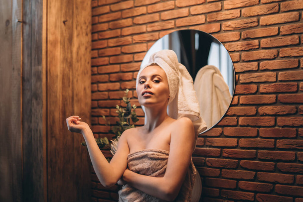 Pretty brunette with towel on her had standing near mirror in the bathroom after shower - Fotoğraf, Görsel