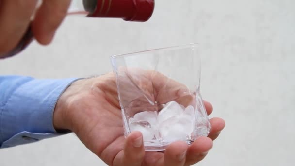 Αρσενικό χέρι ρίχνει και στροβιλίζεται ένα ποτήρι ουίσκι και παγάκια - Πλάνα, βίντεο