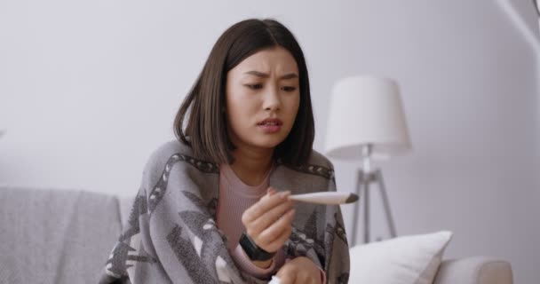 Femme asiatique bouleversée regardant thermomètre avec un résultat de fièvre, s'inquiétant des symptômes du coronavirus, au ralenti - Séquence, vidéo
