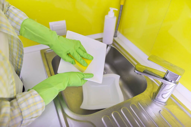 Close-up of womans hand in gloves with sponge detergent washing dirty dishes - 写真・画像