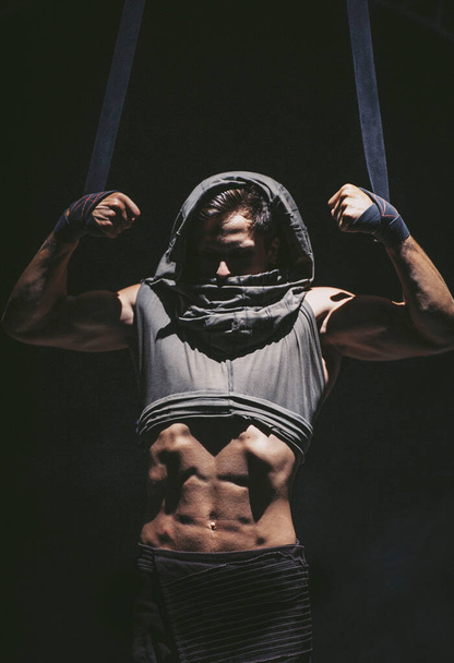 Bodybuilder in hood makes pull-up in ropes - Photo, Image