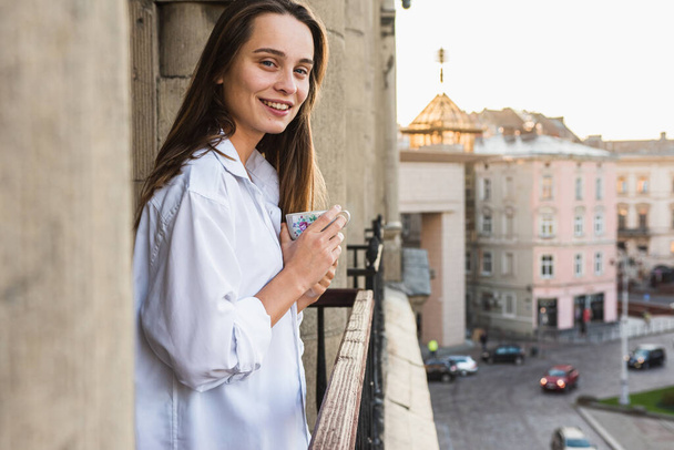 Retrato de una joven feliz, feliz bebiendo café, té de la mañana en el balcón, buena mañana - Foto, Imagen