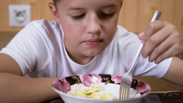Hambriento adolescente come pasta en casa cocina y entrecerraduras fuerte en el disgusto - Imágenes, Vídeo
