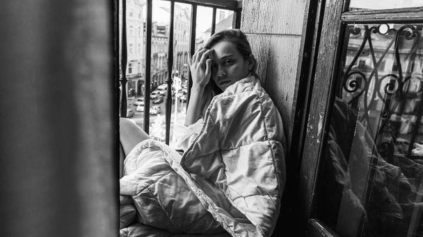 Ragazza felice. Mattina ragazza alba seduta sul balcone avvolto in una coperta luminosa, bella mattina. Concentrazione selettiva. Foto in bianco e nero  - Foto, immagini