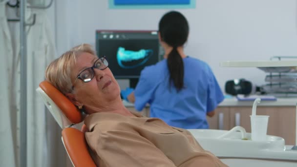 Starší žena dívá na kameru čeká na zubní klinice - Záběry, video