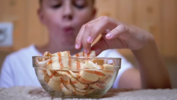 Hongerige tiener zet chips van een plaat in de mond thuis. Jongen eet Fast Food - Video