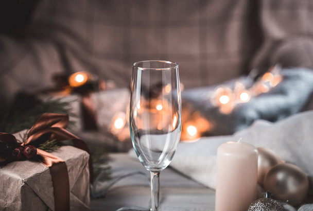 Szklanka szampana na tle świąt Bożego Narodzenia w przytulnej domowej atmosferze wieczorem, ze świecącymi latarniami w tle. - Zdjęcie, obraz