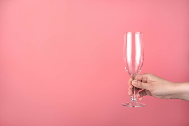 Hand holding an empty champagne glass on a pink background. - Photo, Image