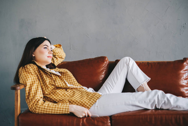 Young calm caucasian stylish woman relaxing lying on comfortable sofa in modern living room, lazy happy woman resting on couch at home. High quality photo - Fotografie, Obrázek