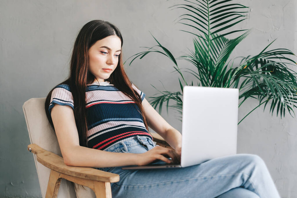 Portrait of beautiful brunette young woman, freelancer working distantly at home, looking at laptop screen on video call or chat and typing on keyboard. High quality photo - Φωτογραφία, εικόνα