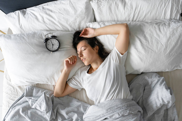 Top view of a girl sleeping next to an alarm clock. Time to wake up. On the wake-up clock 7 a.m. Deep sleep - Fotó, kép