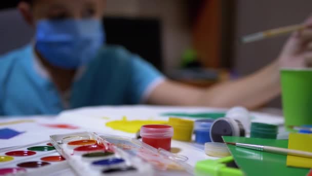 Enfant en masque assis à la table dans la chambre et peinture tableau avec pinceau avec de la peinture verte - Séquence, vidéo