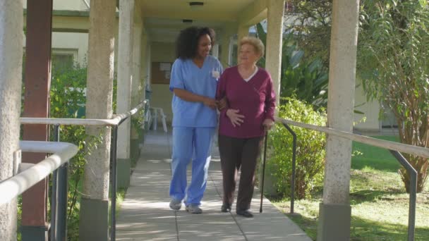 Αργή κίνηση της αφρικανικής γυναίκα γιατρός βοηθώντας ηλικιωμένη γυναίκα με το μπαστούνι στο κήπο του νοσοκομείου - Πλάνα, βίντεο