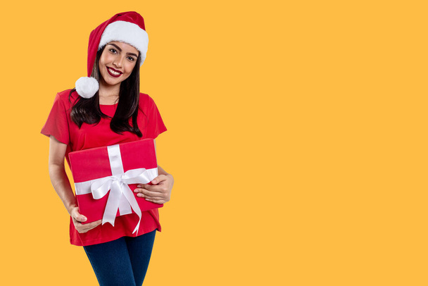 Γυναίκα με χριστουγεννιάτικο καπέλο κρατώντας ένα δώρο, απομονώνονται σε κίτρινο φόντο - Φωτογραφία, εικόνα