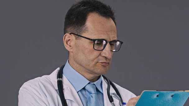 Close-up serious doctor in medical uniform writes patient diagnosis on clipboard - Photo, image