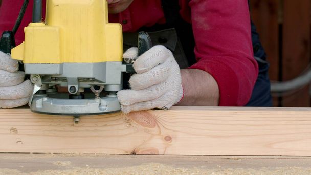 Csucasian ξυλουργός επεξεργάζεται δοκό ξύλου με μηχανή άλεσης. - Φωτογραφία, εικόνα