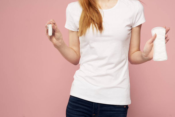 Woman with a pad in her hand on a pink background jeans T-shirt tampons hygiene frequency - Photo, Image
