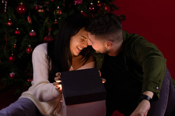 romantisches Liebespaar, das sich beim Öffnen des magischen Weihnachtsgeschenks sanft umarmt - Foto, Bild