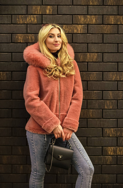spring summer trend. Fashionable woman in pink fur coat at brick wall. cold season. Autumn or winter look. beautiful stylish woman walking in pink coat. holding purse in hands. street style - Fotoğraf, Görsel