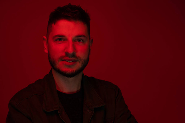 Low key portrait of bearded chubby young man in red light on dark backdrop - Photo, Image