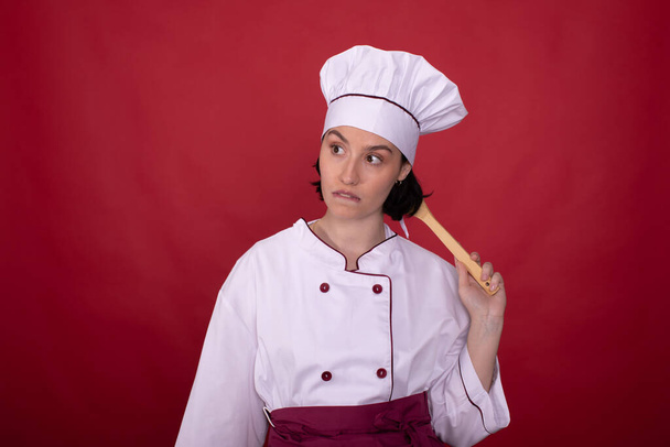atraktivní sexy žena kuchař kousání rty poškrábání hlavu s dřevěnou špachtle - Fotografie, Obrázek