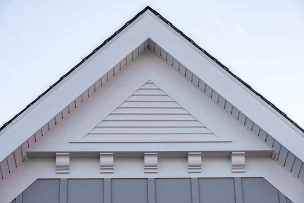 Pignon avec revêtement vertical en vinyle gris, évent à pignon en PVC à montage vertical classique sur un grenier à toit incliné dans un quartier américain unifamilial aux États-Unis avec supports décoratifs blancs - Photo, image