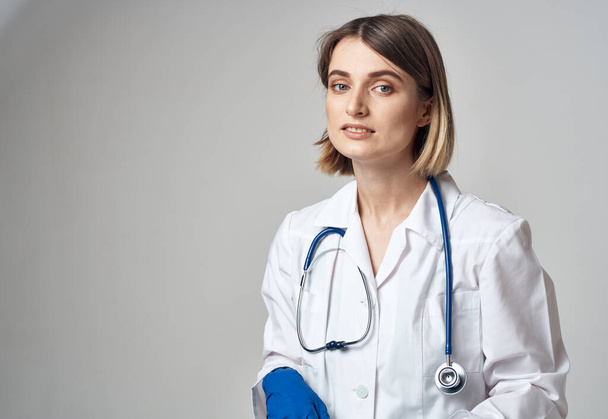 Porträt einer Krankenschwester in Handschuhen und medizinischem Gewand auf hellem Hintergrund - Foto, Bild