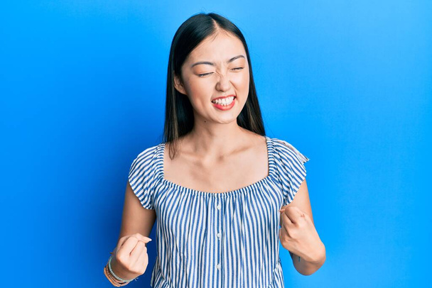 Young chinese woman wearing casual striped t-shirt very happy and excited doing winner gesture with arms raised, smiling and screaming for success. celebration concept.  - Photo, Image