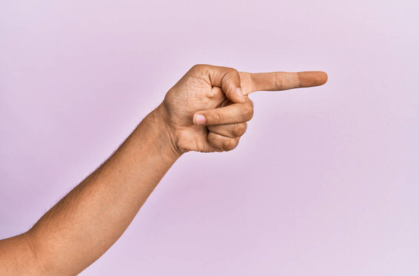 Pembe izole edilmiş arka plan üzerinde beyaz bir gencin eli ve kolu işaret ediyor, işaret parmağı yana, bir seçim öneriyor ve seçiyor  - Fotoğraf, Görsel