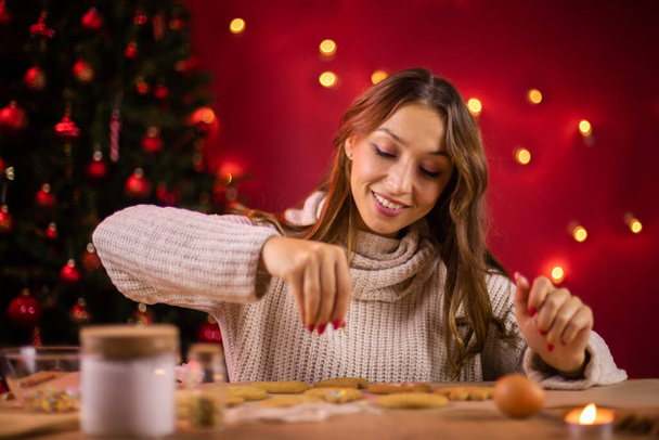 Świąteczne pieczenie. ładny uśmiech młoda kobieta dekorowanie ciasteczka świąteczne - Zdjęcie, obraz