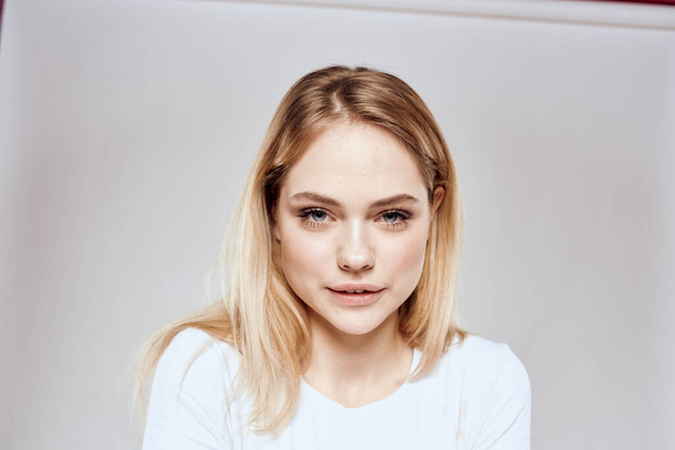 vrolijk blond in een wit t-shirt gebaren met haar handen licht achtergrond - Foto, afbeelding