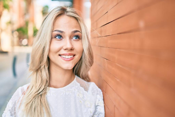 Jeune fille caucasienne souriant heureux penché sur le mur à la rue de la ville. - Photo, image