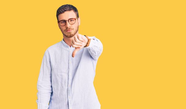 Handsome young man with bear wearing elegant business shirt and glasses looking unhappy and angry showing rejection and negative with thumbs down gesture. bad expression.  - Photo, Image