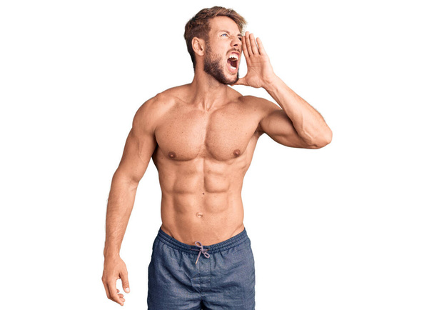 Young caucasian man standing shirtless shouting and screaming loud to side with hand on mouth. communication concept.  - Photo, Image
