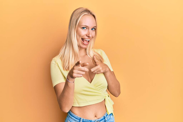 Jeune fille blonde portant des vêtements décontractés pointant les doigts vers la caméra avec un visage heureux et drôle. bonne énergie et vibes.  - Photo, image