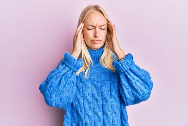 Jong blond meisje draagt wol winter trui met de hand op het hoofd voor pijn in het hoofd omdat stress. lijden aan migraine.  - Foto, afbeelding