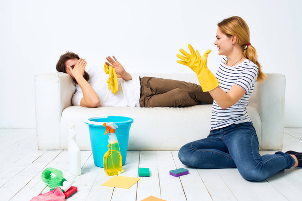 The wife cleans up while the husband lies on the couch interior housework - Zdjęcie, obraz