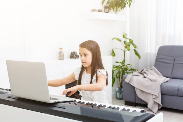 Hezký mladý hudebník hrající doma na klasickém digitálním klavíru během online hodiny doma, společenská vzdálenost během karantény, sebeizolace, koncepce on-line vzdělávání - Fotografie, Obrázek