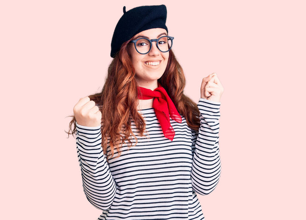 Young beautiful woman wearing french look with beret screaming proud, celebrating victory and success very excited with raised arms  - Fotografie, Obrázek