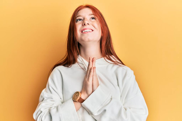 Young red head girl wearing casual sweatshirt begging and praying with hands together with hope expression on face very emotional and worried. begging.  - Photo, Image