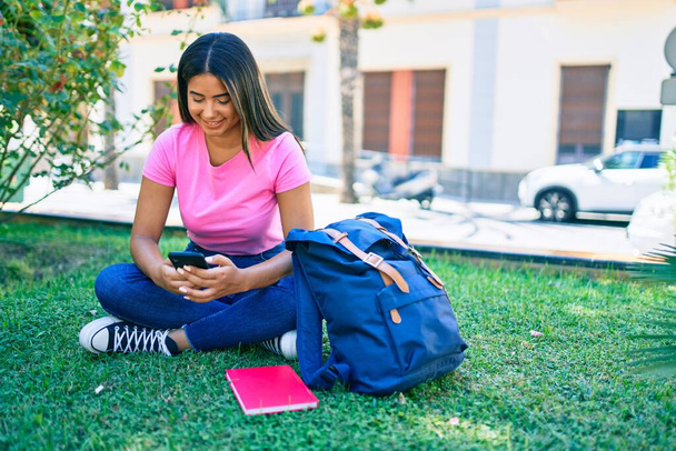 Молода латинська студентка посміхається щаслива, використовуючи смартфон в університетському містечку
. - Фото, зображення