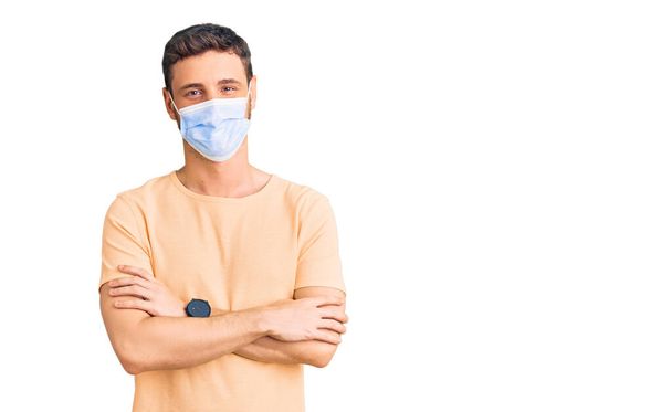 Handsome young man with bear wearing medical mask for coronavirus happy face smiling with crossed arms looking at the camera. positive person.  - Foto, imagen