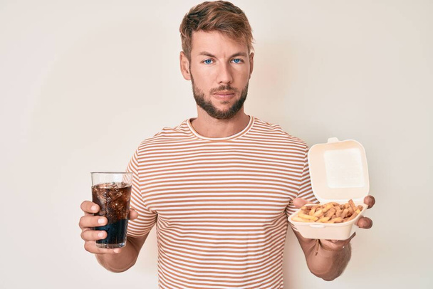Hombre joven caucásico comiendo comida rápida relajado con expresión seria en la cara. simple y natural mirando a la cámara.  - Foto, imagen