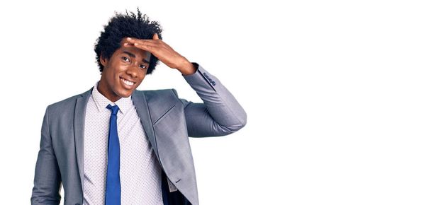 Handsome african american man with afro hair wearing business jacket very happy and smiling looking far away with hand over head. searching concept.  - Photo, Image