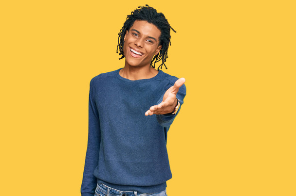 Молодий афроамериканець у повсякденному зимовому светрі усміхається, пропонуючи долоні допомогу і прийняття.  - Фото, зображення